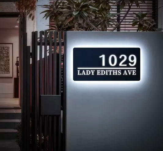 Modern rectangular custom LED house address sign glowing white with number and street name on wall at night