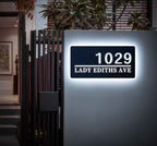Modern rectangular custom LED house address sign glowing white with number and street name on wall at night
