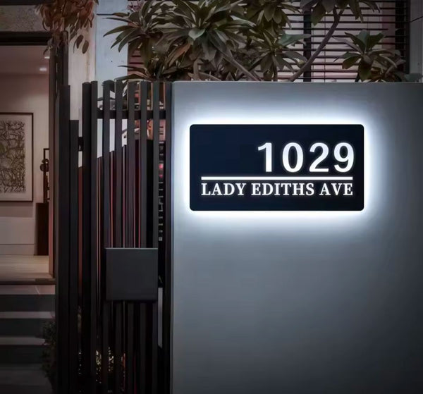 Modern rectangular custom LED house address sign glowing white with number and street name on wall at night