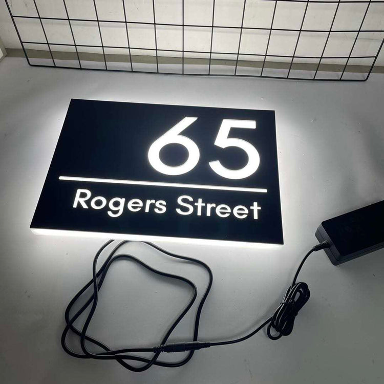 House number sign with '65 Rogers Street' on a black background, connected to a power adapter.