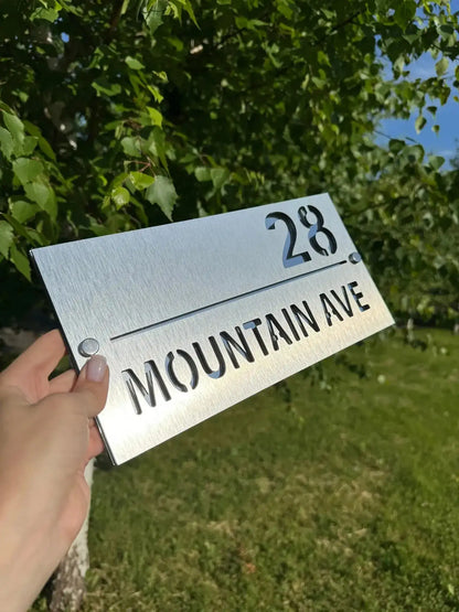 Handheld personalised stainless steel address sign with brushed finish showing 28 Mountain Ave text outdoors
