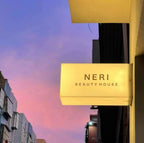 Illuminated double-sided acrylic LED lightbox sign for NERI Beauty House mounted outside building at dusk.