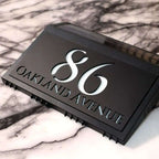 Modern black solar acrylic house sign with illuminated number 86 and Oakland Avenue address engraving.
